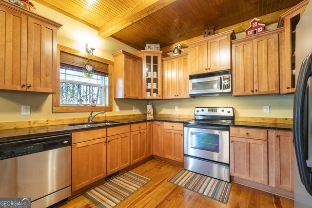 kitchen with beam ceiling, sink, stainless steel appliances, dark stone countertops, and light hardwood / wood-style floors