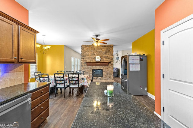 kitchen with appliances with stainless steel finishes, backsplash, dark wood-type flooring, decorative light fixtures, and a fireplace