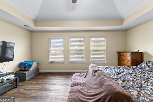 bedroom featuring multiple windows, dark hardwood / wood-style flooring, a raised ceiling, and ceiling fan