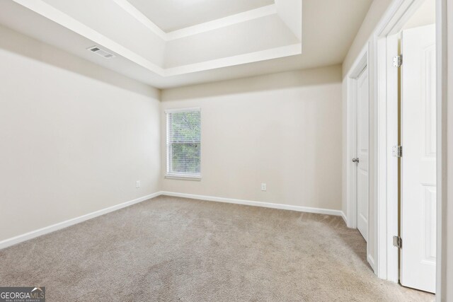 unfurnished bedroom featuring light carpet and a tray ceiling