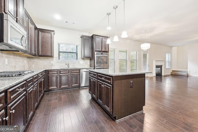 kitchen with decorative light fixtures, a center island, dark brown cabinetry, and appliances with stainless steel finishes