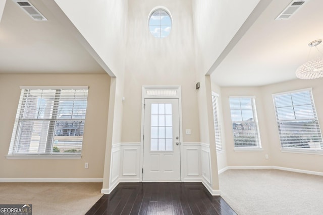 foyer with a wealth of natural light, dark carpet, and a notable chandelier