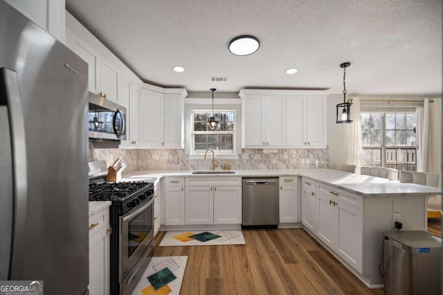 kitchen with kitchen peninsula, appliances with stainless steel finishes, a textured ceiling, sink, and hanging light fixtures