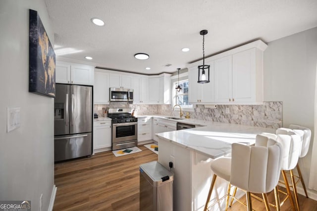 kitchen with white cabinets, hanging light fixtures, light stone countertops, dark hardwood / wood-style flooring, and stainless steel appliances