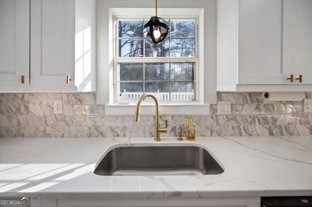 kitchen with light stone countertops, decorative backsplash, sink, pendant lighting, and white cabinetry