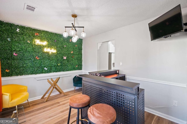 bar featuring stainless steel fridge with ice dispenser, wood-type flooring, and a textured ceiling