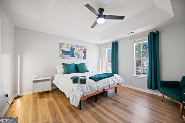 bedroom featuring a textured ceiling, ceiling fan, light hardwood / wood-style flooring, and a tray ceiling