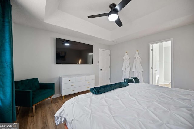 bedroom with a raised ceiling, connected bathroom, ceiling fan, and wood-type flooring