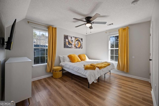 bedroom with hardwood / wood-style floors, a textured ceiling, vaulted ceiling, and ceiling fan