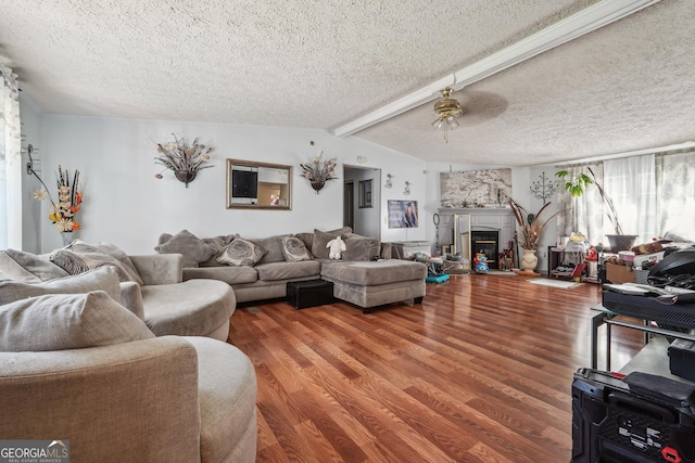 living room featuring lofted ceiling with beams, ceiling fan, a textured ceiling, a fireplace, and wood-type flooring