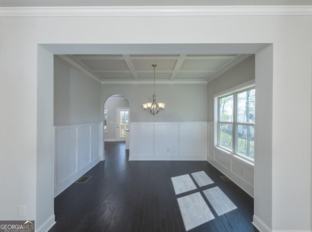 unfurnished dining area with dark wood-type flooring, an inviting chandelier, beam ceiling, coffered ceiling, and ornamental molding