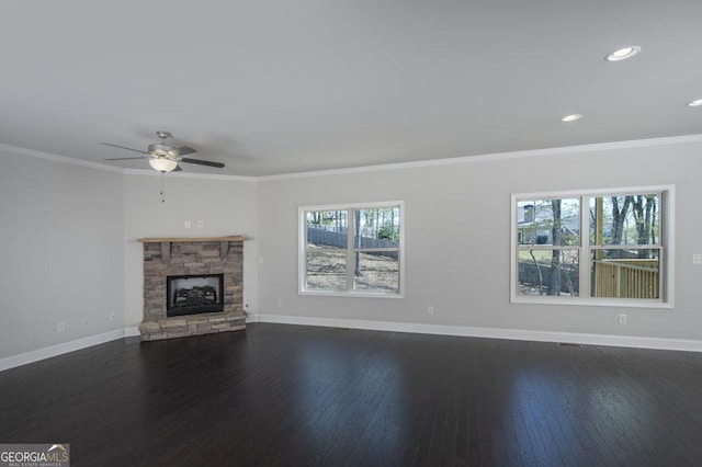 unfurnished living room featuring crown molding, a stone fireplace, dark hardwood / wood-style flooring, and ceiling fan