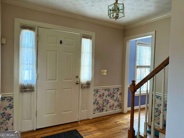 foyer featuring a textured ceiling, light hardwood / wood-style floors, an inviting chandelier, and ornamental molding