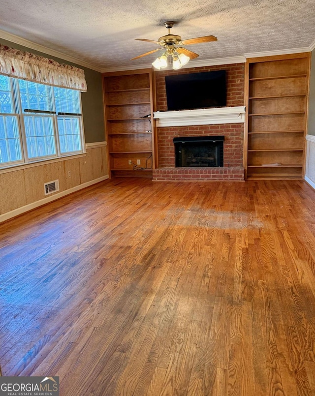 unfurnished living room with a textured ceiling, crown molding, built in features, a fireplace, and wood walls