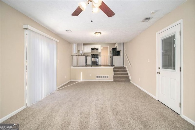 unfurnished living room featuring ceiling fan, light colored carpet, and a textured ceiling