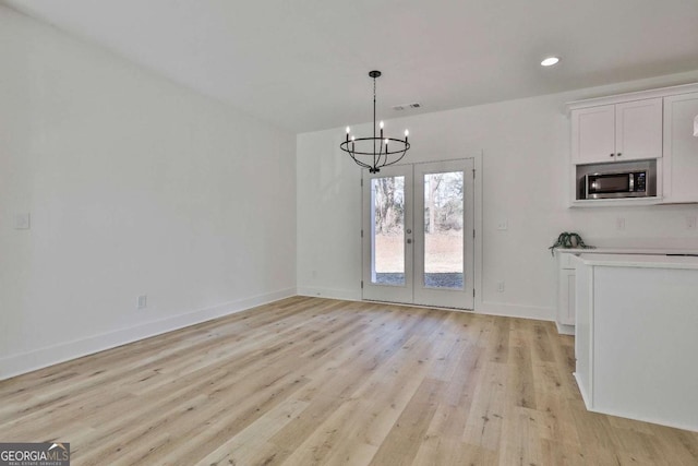 unfurnished dining area featuring french doors, light hardwood / wood-style floors, and a notable chandelier