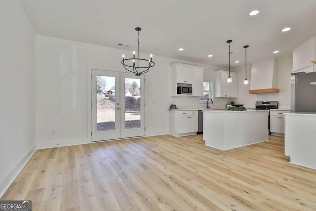 kitchen featuring premium range hood, stainless steel appliances, decorative light fixtures, white cabinetry, and a kitchen island