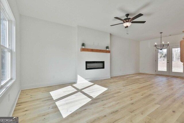 unfurnished living room with ceiling fan with notable chandelier, french doors, and light wood-type flooring