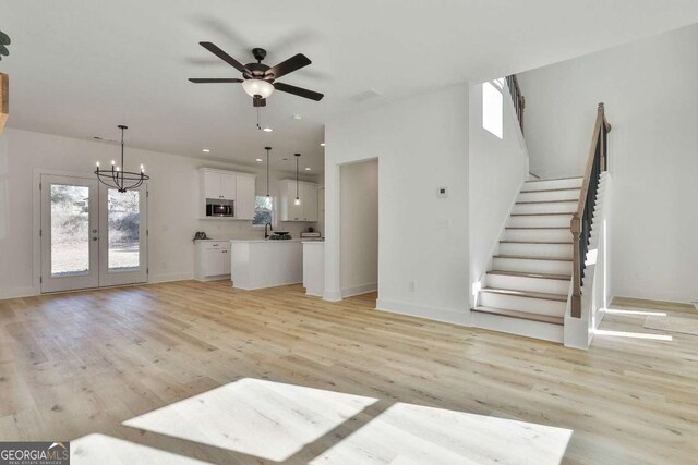 unfurnished living room with plenty of natural light, light wood-type flooring, ceiling fan with notable chandelier, and french doors