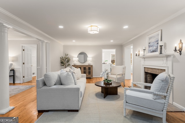 living room featuring decorative columns, a brick fireplace, light wood-type flooring, and ornamental molding