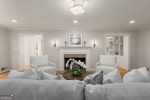 living room featuring built in features, light hardwood / wood-style floors, a brick fireplace, and crown molding