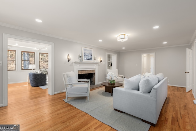 living room with crown molding, built in features, light hardwood / wood-style floors, and a brick fireplace