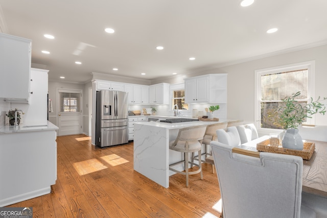 kitchen with stainless steel fridge, crown molding, light hardwood / wood-style flooring, white cabinets, and a breakfast bar area