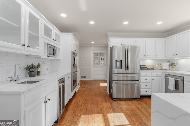 kitchen with light stone countertops, appliances with stainless steel finishes, sink, light hardwood / wood-style floors, and white cabinetry