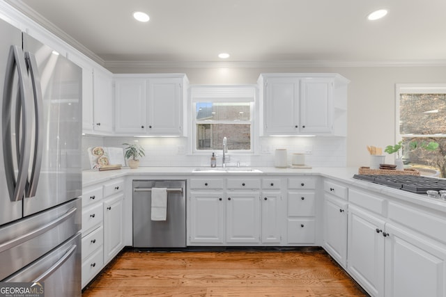 kitchen with white cabinets, crown molding, sink, light hardwood / wood-style floors, and stainless steel appliances