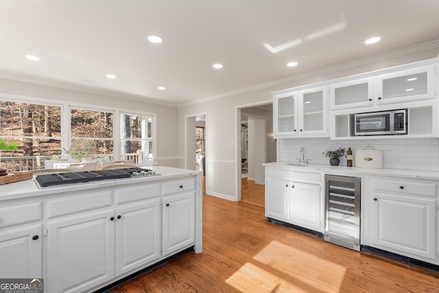 kitchen featuring beverage cooler, tasteful backsplash, appliances with stainless steel finishes, white cabinets, and light wood-type flooring