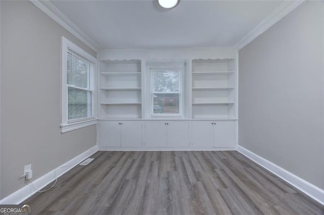 empty room with built in shelves, light hardwood / wood-style floors, and ornamental molding