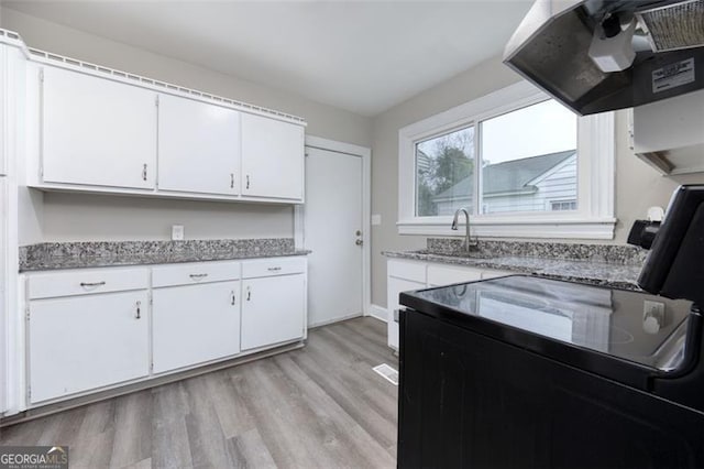 kitchen featuring stove, white cabinets, sink, light wood-type flooring, and range hood