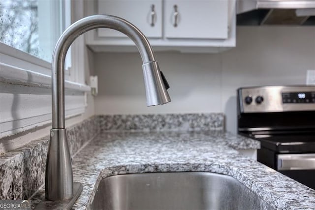 interior details featuring ventilation hood, white cabinets, stainless steel electric stove, sink, and light stone counters