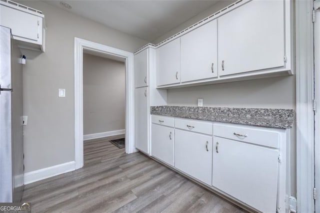 kitchen featuring stainless steel refrigerator, white cabinets, light hardwood / wood-style floors, and stone countertops