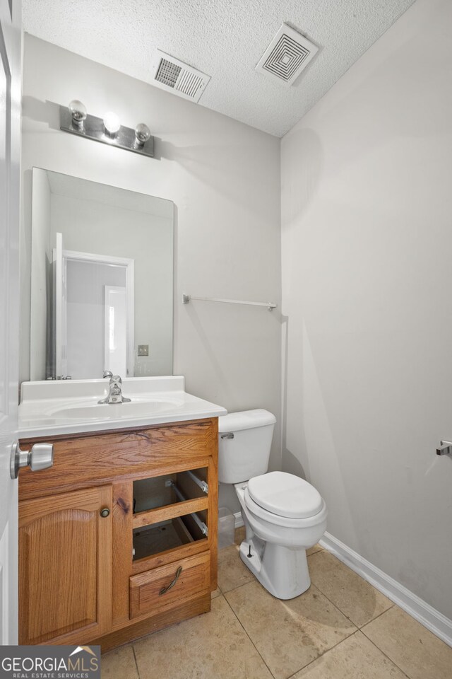 bathroom featuring tile patterned flooring, vanity, toilet, and a textured ceiling