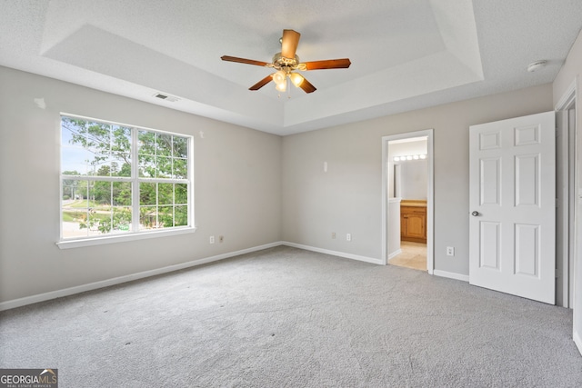 unfurnished bedroom with connected bathroom, ceiling fan, a textured ceiling, a tray ceiling, and light carpet