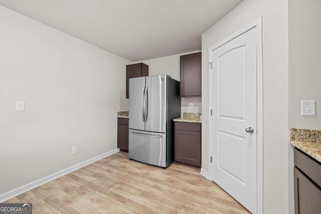 kitchen with dark brown cabinets, light stone counters, stainless steel refrigerator, and light hardwood / wood-style flooring