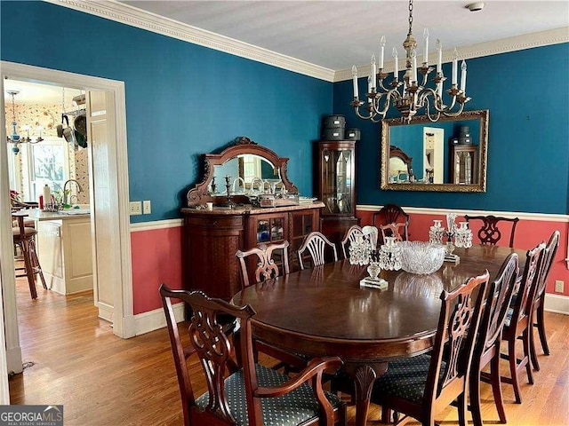 dining space featuring sink, ornamental molding, a chandelier, and light wood-type flooring