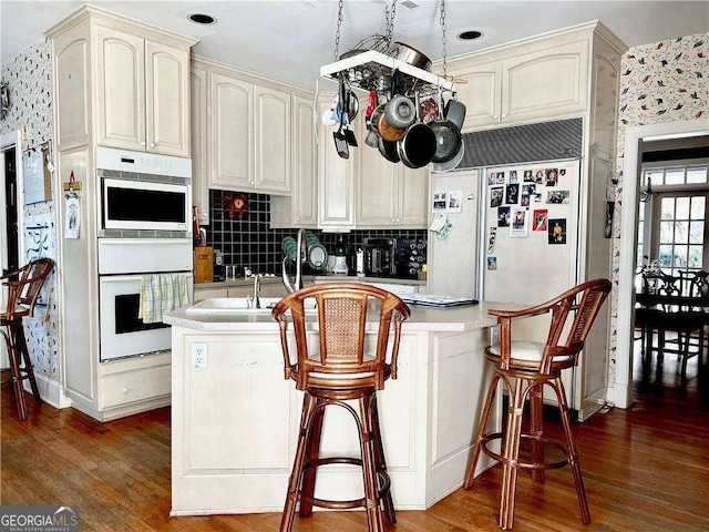 kitchen featuring double oven, cream cabinetry, dark hardwood / wood-style floors, and backsplash