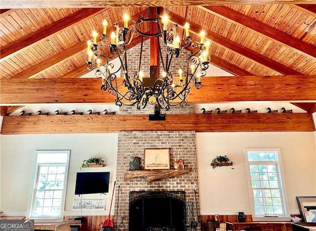 living room featuring lofted ceiling with beams, a brick fireplace, plenty of natural light, and a chandelier