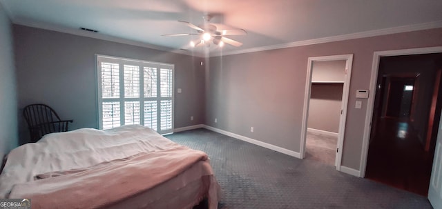 bedroom featuring ceiling fan, a walk in closet, a closet, dark carpet, and ornamental molding