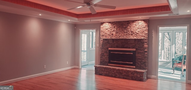 unfurnished living room with a tray ceiling, ceiling fan, a fireplace, and light hardwood / wood-style flooring