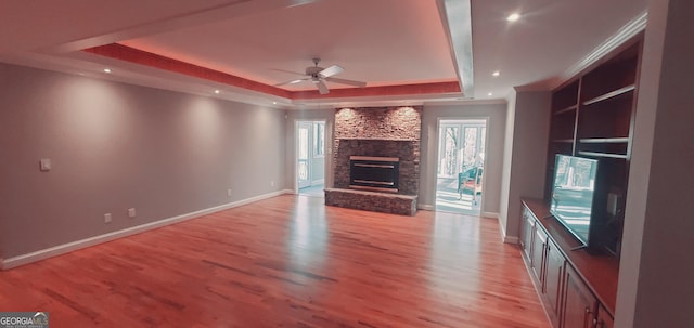 unfurnished living room with built in shelves, a raised ceiling, ceiling fan, a fireplace, and light hardwood / wood-style floors