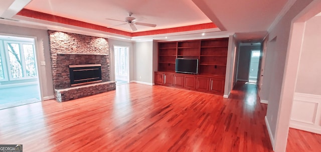 unfurnished living room with ceiling fan, a stone fireplace, a raised ceiling, and light hardwood / wood-style flooring