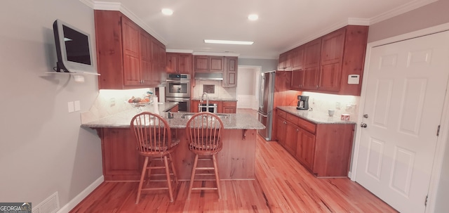 kitchen with crown molding, appliances with stainless steel finishes, light hardwood / wood-style floors, kitchen peninsula, and a breakfast bar area