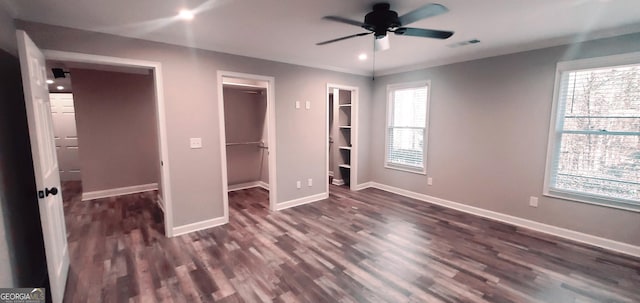 unfurnished bedroom featuring a spacious closet, ceiling fan, and dark wood-type flooring