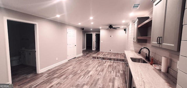 kitchen featuring hardwood / wood-style flooring, light stone counters, ceiling fan, and sink