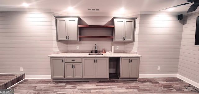 kitchen with gray cabinets, light stone counters, sink, and dark wood-type flooring