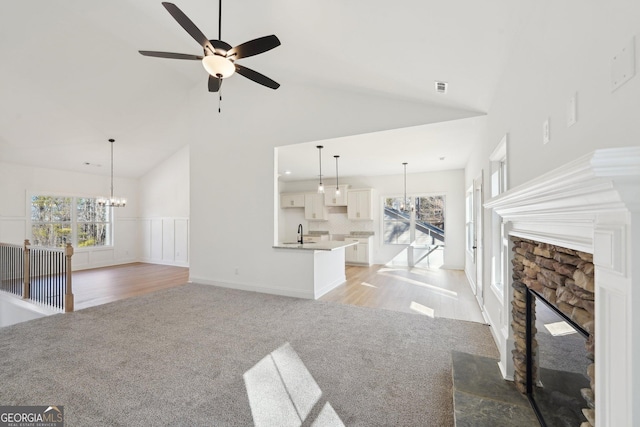 unfurnished living room with ceiling fan with notable chandelier, a fireplace, sink, and light carpet