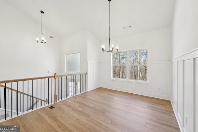 unfurnished dining area with an inviting chandelier, vaulted ceiling, and light hardwood / wood-style flooring